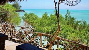 Een houten terras met rieten dak, met uitzicht op turquoise water en weelderige begroeiing.