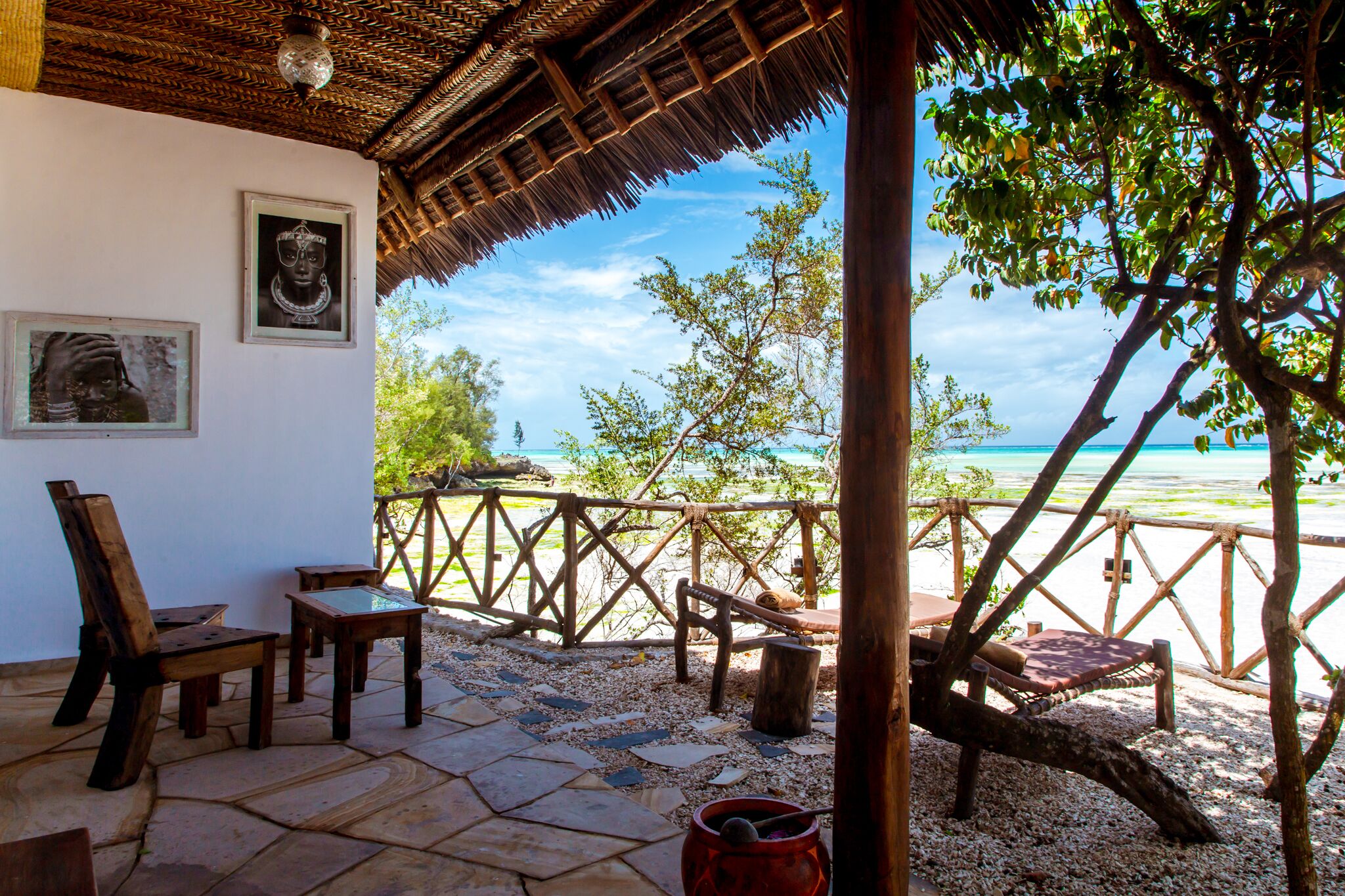 A wooden deck with chairs and a table, overlooking a beach with a clear view of the sea.