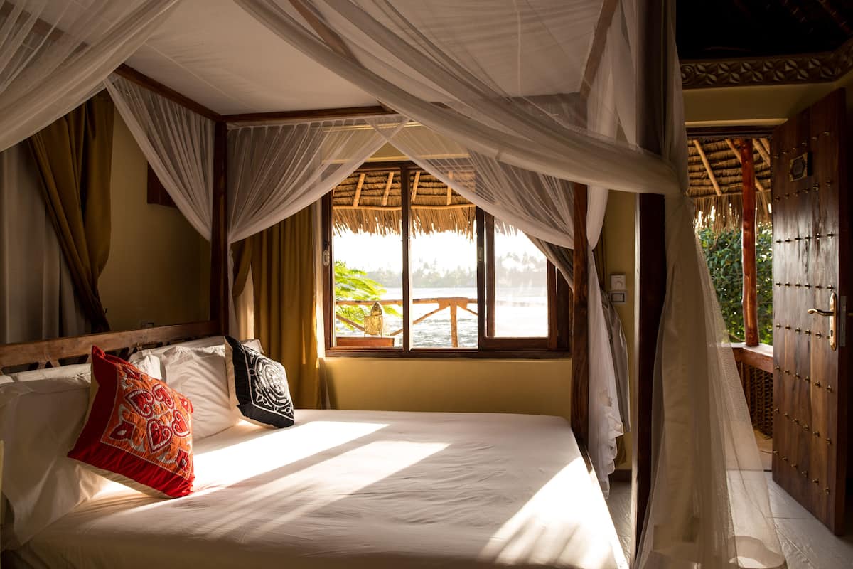 Een kamer met een bed, een raam met uitzicht op zee en een houten deur.