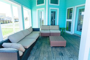 Un portico riparato con una combinazione di colori blu e bianco, con un divano in vimini e un tavolino.