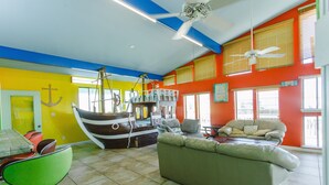 Una habitación luminosa y de colores llamativos, con una cama grande con motivos marinos, un sofá y un comedor con sillas.