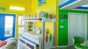 Una habitación con una cama individual superpuesta, un ventilador de techo, una silla verde y una puerta que dice 'BEACH'.