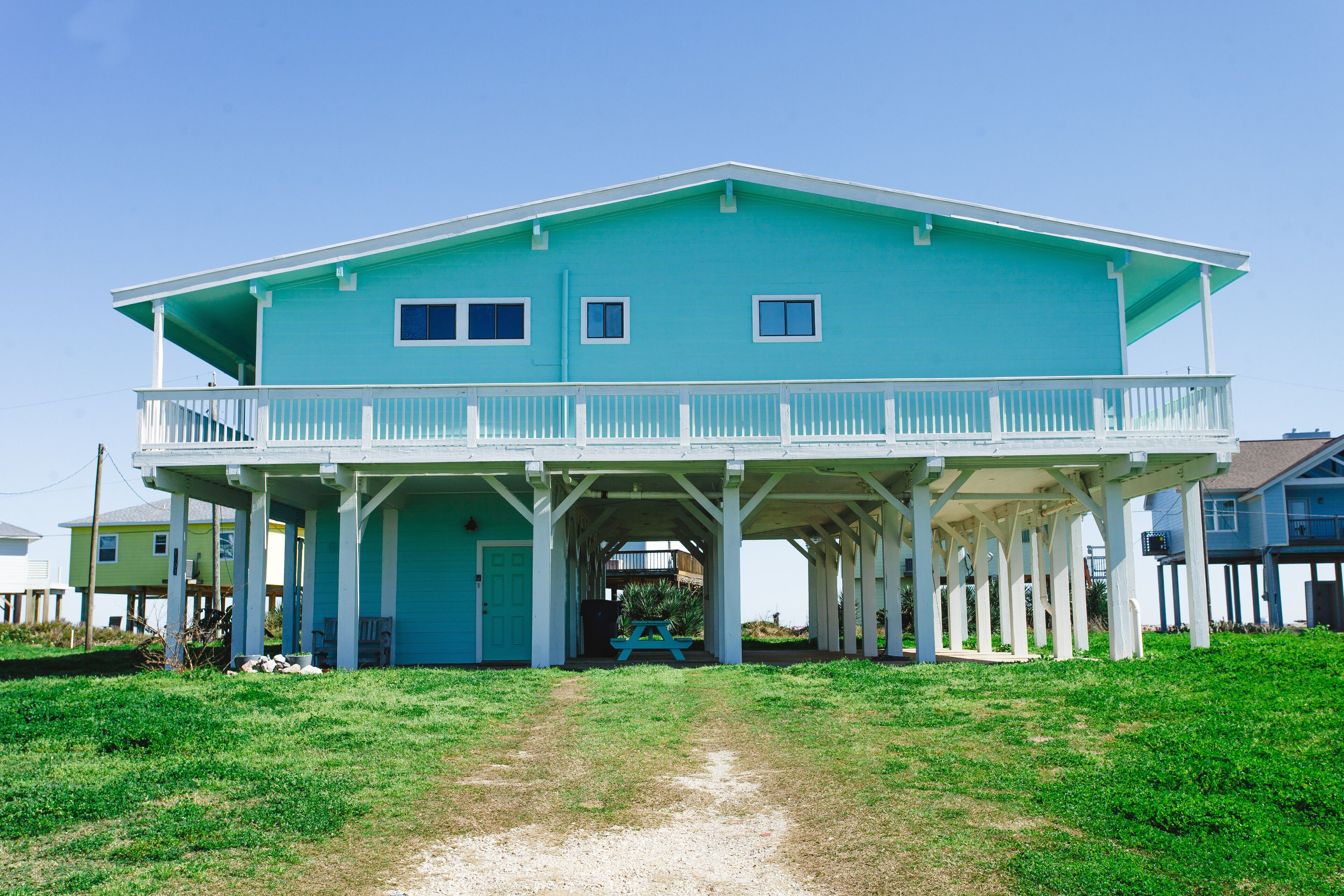 A two-story house with a balcony, a covered porch, and a sandy driveway.