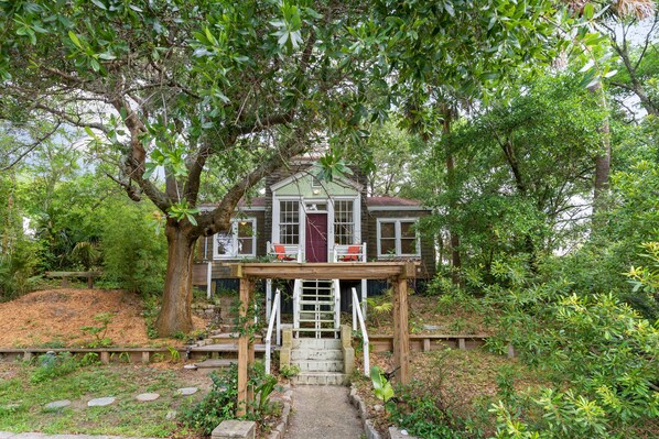 A house with a wooden deck, a red door, and a staircase leading to the entrance.
