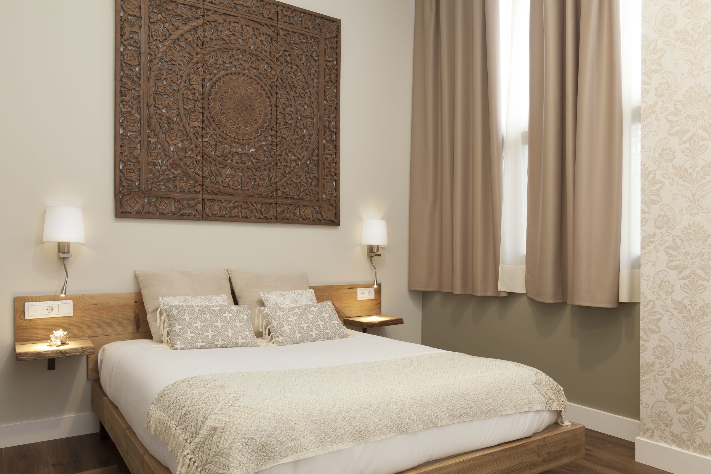 Un dormitorio con una cama grande, dos lámparas de noche, un adorno en la pared y una ventana con cortinas.