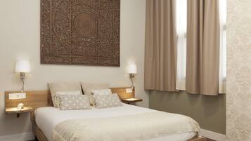 Un dormitorio con una cama grande, dos lámparas de noche, un adorno en la pared y una ventana con cortinas.