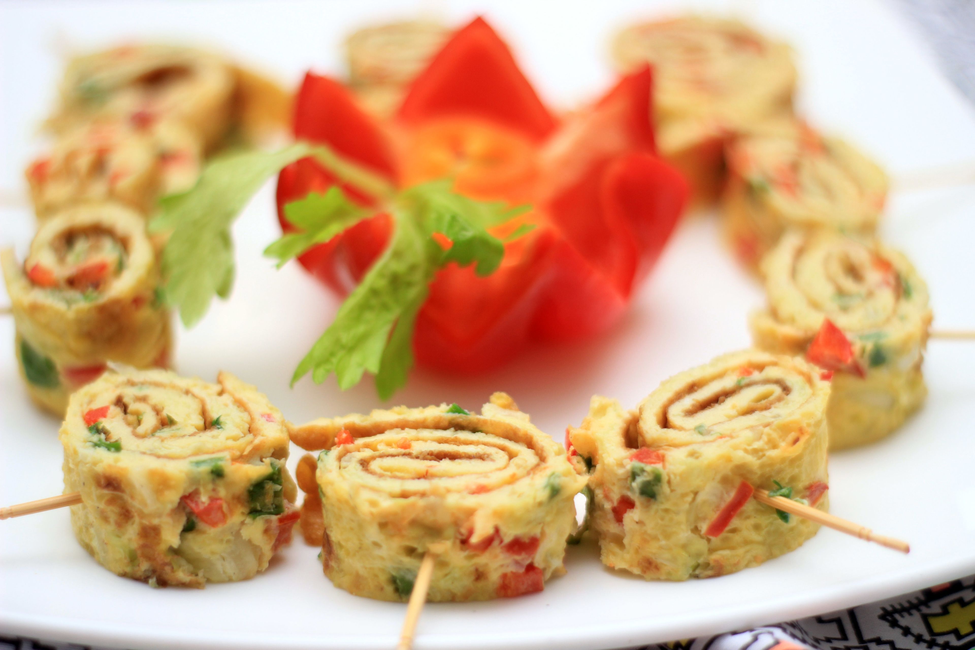 Un plato de aperitivos enrollados con palillos, adornado con perejil y rodeado por una loncha de pimiento rojo.