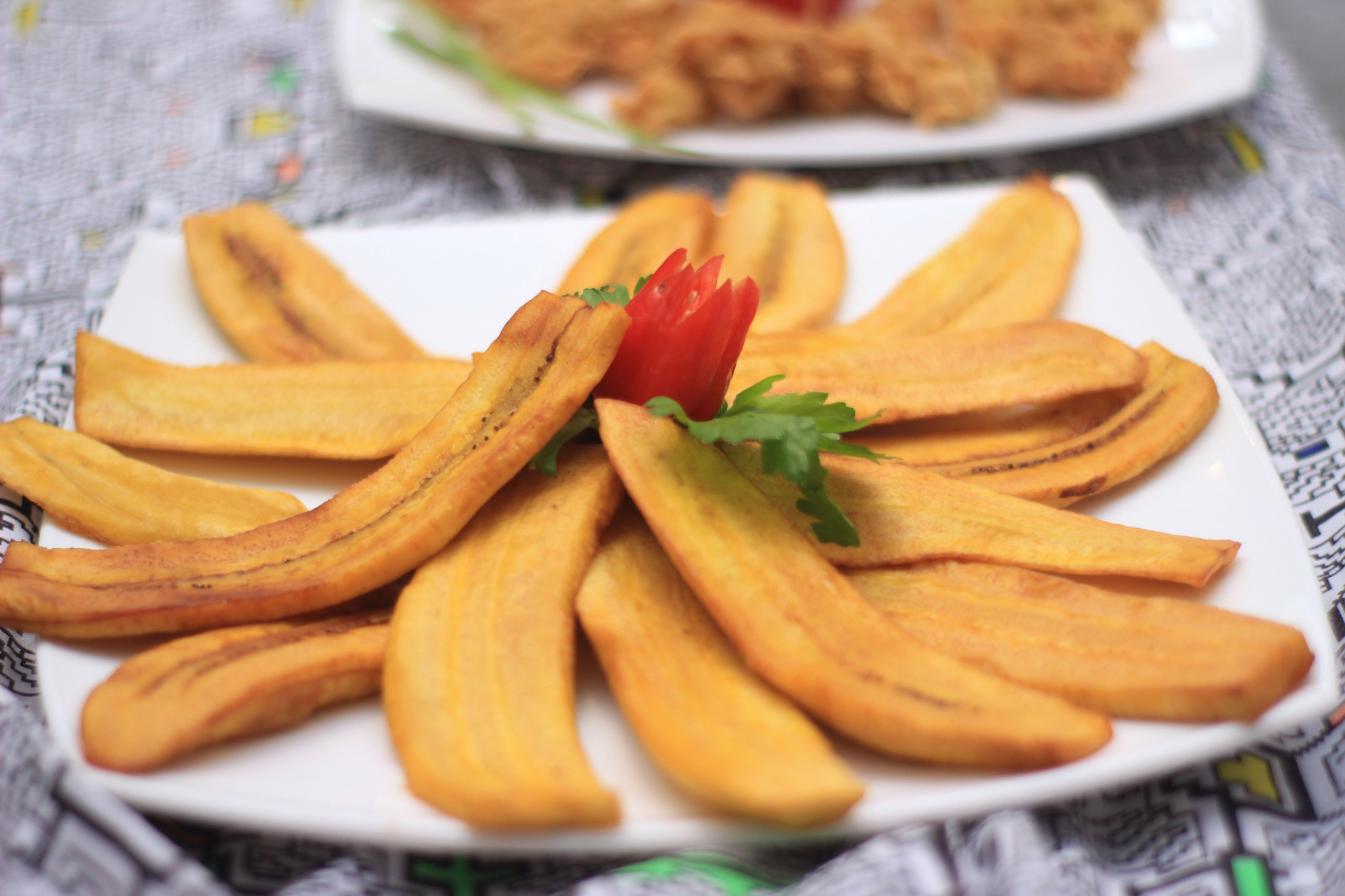 Een bord gebakken plantains, versierd met een plakje tomaat en peterselie.