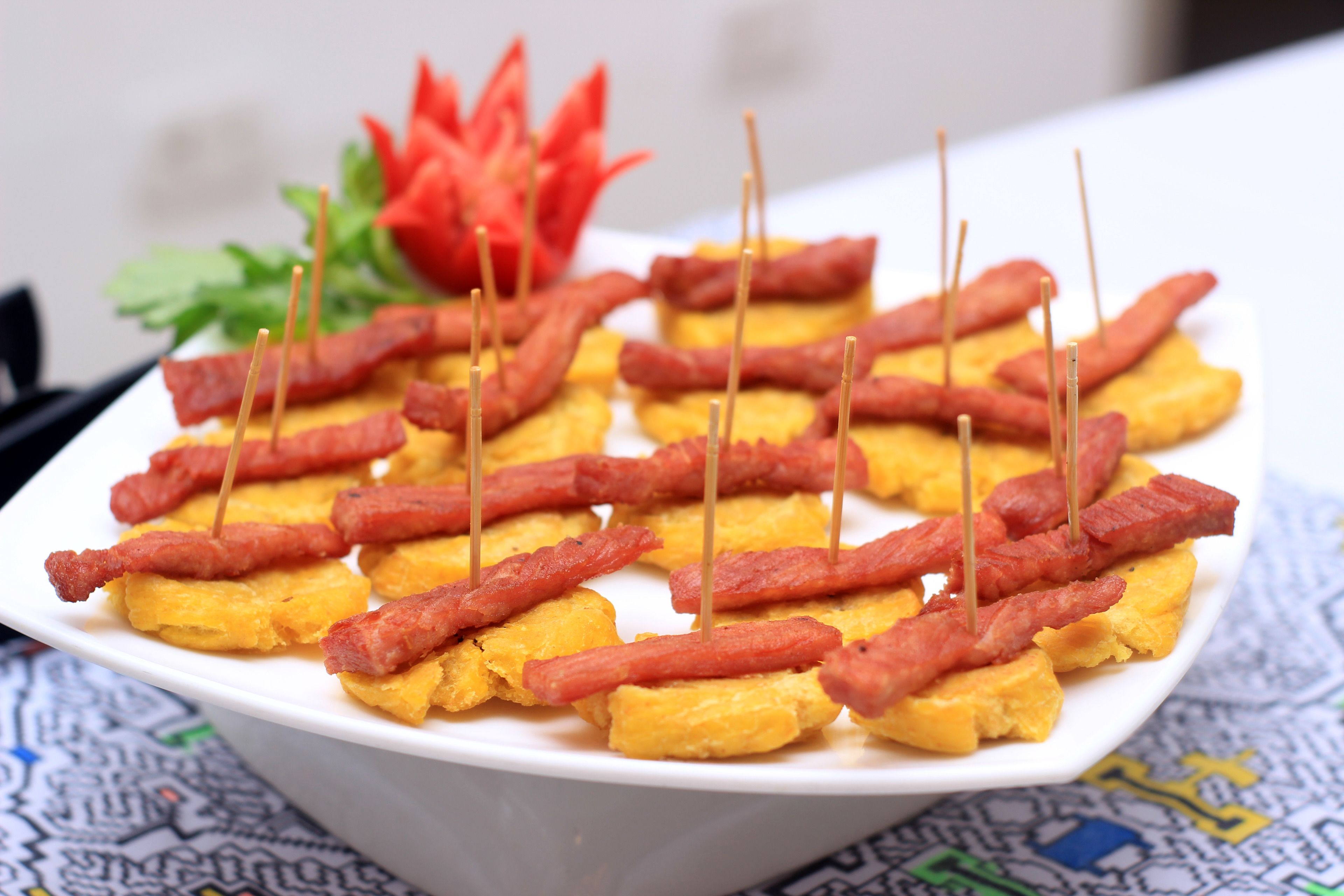 Un plato blanco con alimentos, incluyendo trozos amarillos y tiras rojas, sobre un mantel estampado.