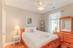 Quarto bem arrumado com uma cama de madeira, uma mesa de cabeceira com abajur, uma estante com objetos decorativos e um espelho grande.
