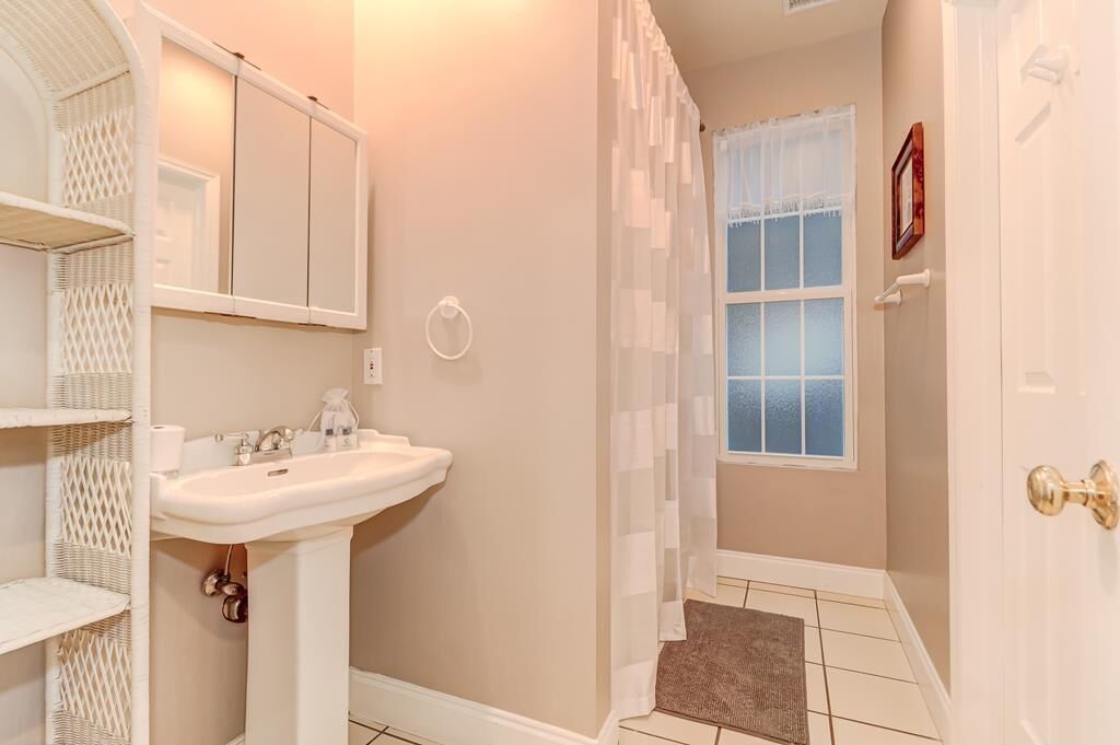 A bathroom with a white sink, a mirror, a shower curtain, and a window.
