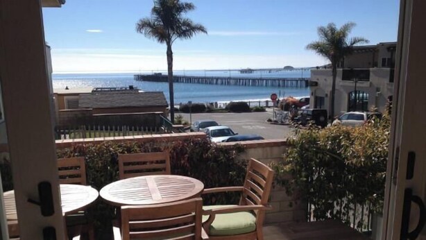 Eine Holzdar Terrasse mit Tisch und Stühlen mit Blick auf einen Strand und einen Steg.