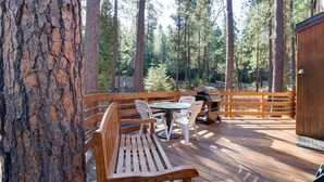 A wooden deck with a table and chairs, surrounded by tall trees. - Basecamp for endless adventure, perfect Black Butte location - Hot Tub! (Sisters)