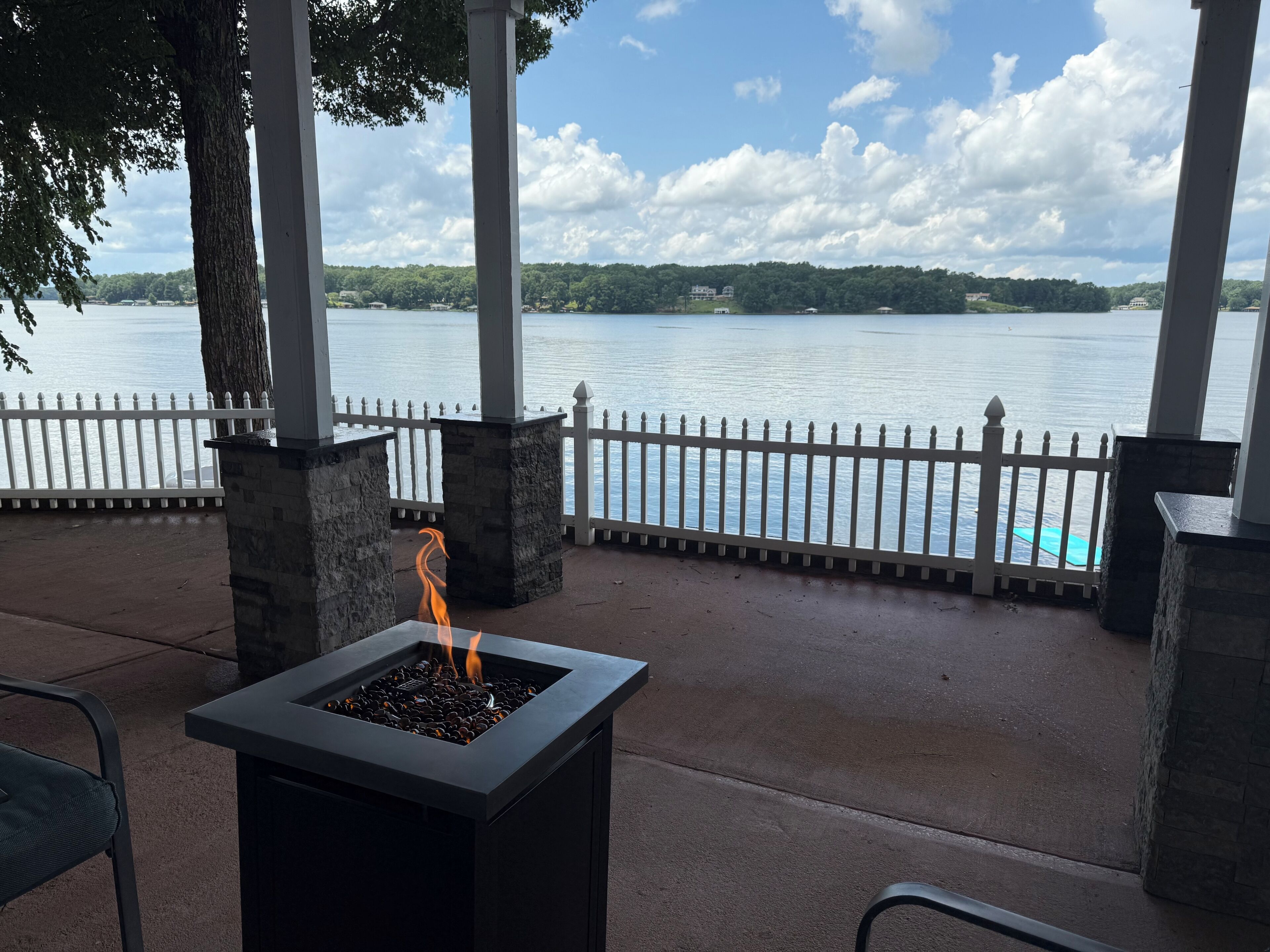 A fire feature with a view of a lake and a white fence.