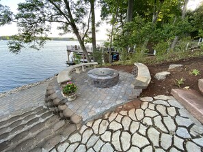 A stone patio with a circular fire pit, surrounded by a curved stone bench and a planter with flowers. - Main Lake Luxury and spectacular panoramic views! Sleeps 8! (Macon)