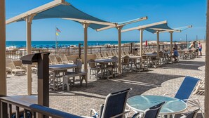 A beachside restaurant with outdoor seating, tables, and umbrellas.