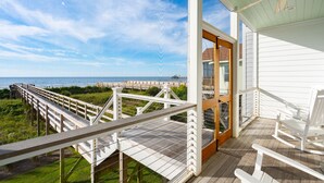 Une terrasse en bois offrant une vue sur l’océan, une porte vitrée donnant sur un porche et un ventilateur de plafond en bois.