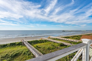 A beach with a wooden boardwalk, grassy areas, and a pier extending into the water.