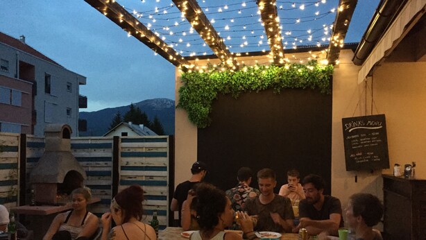 A group of people dining outdoors at a restaurant with string lights overhead and a menu board visible. - Falling Lakes Hostel (Plitvicka Jezera)