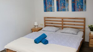 A bedroom with a wooden bed, two bedside tables, a lamp, and three abstract paintings on the wall. - Falling Lakes Hostel (Plitvicka Jezera)