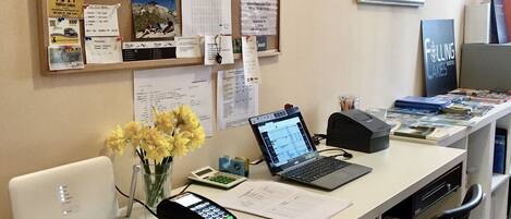 A reception desk with a laptop, a payment terminal, and a vase of flowers.
