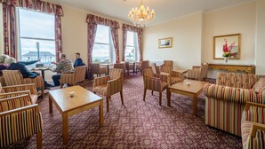 A hotel lounge with striped armchairs, a chandelier, and large windows offering a view of the sea. - Russell Hotel (Weymouth)
