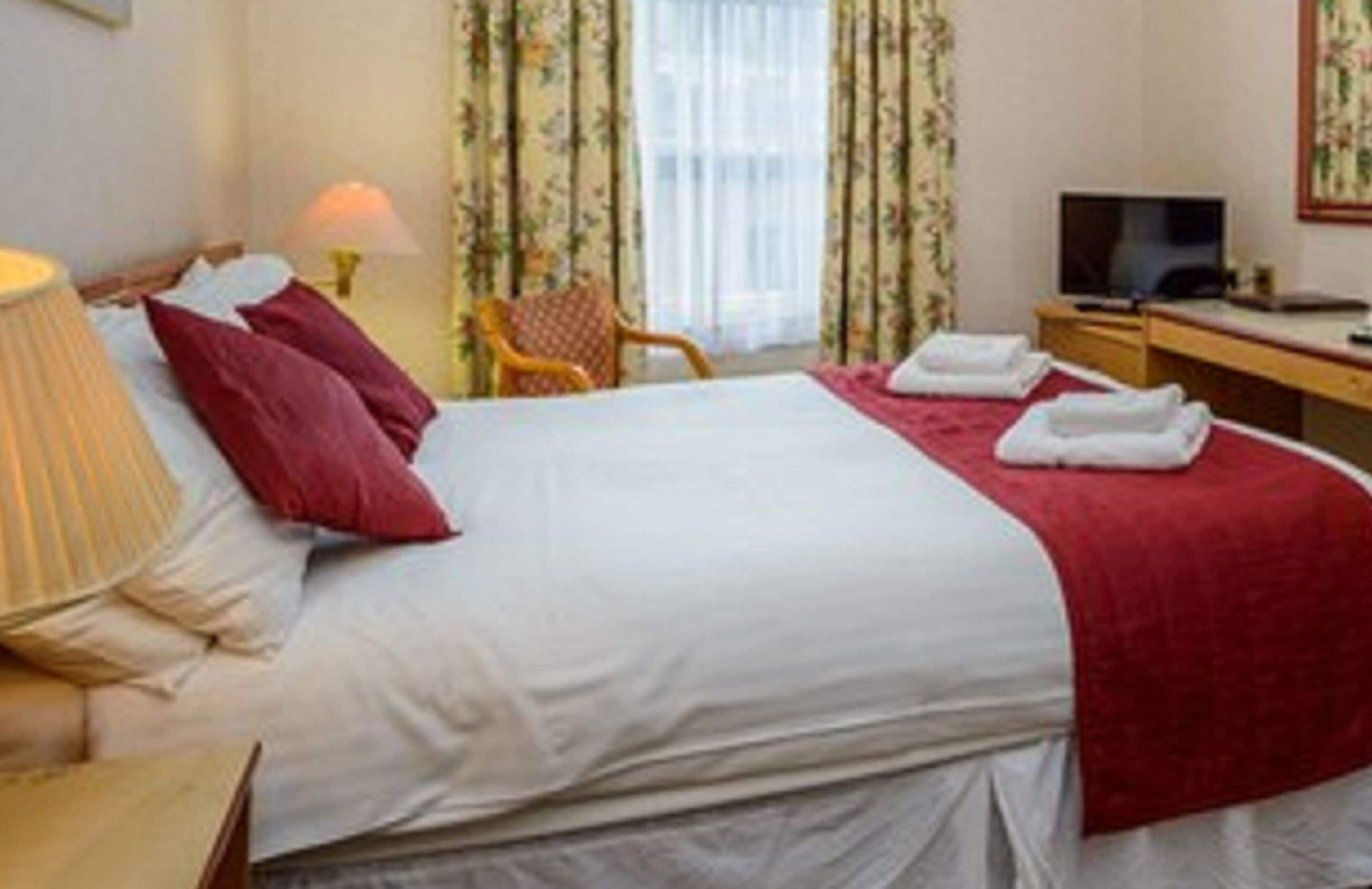 A hotel room with a bed, a desk, a chair, a television, and a window with curtains.