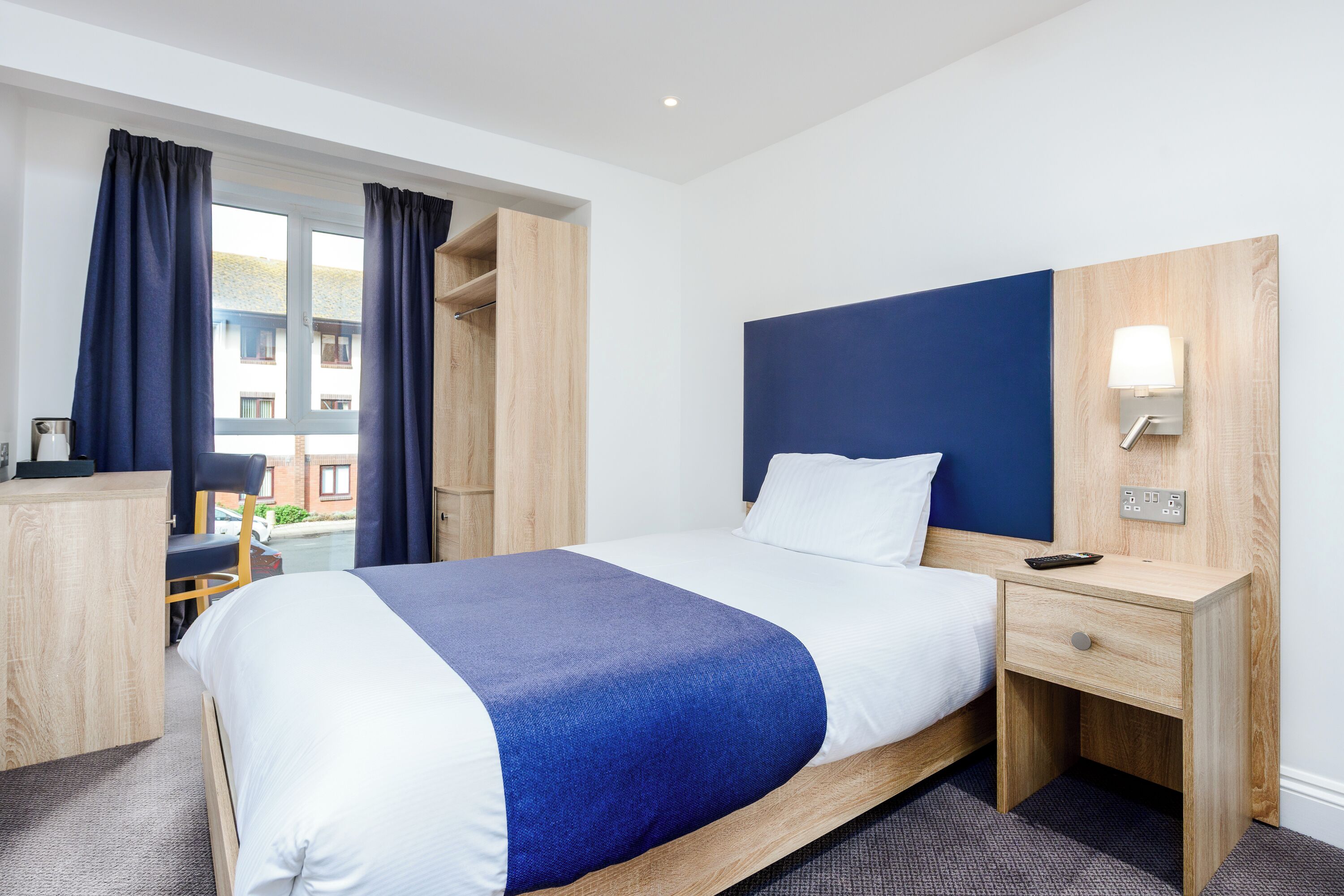 Ein Hotelzimmer mit Bett, Schreibtisch, Stuhl und einem Fenster mit Vorhängen.
