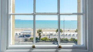 A view through a window of a beachside area with a clear sky, a sandy beach, and a few people walking. - Russell Hotel (Weymouth)