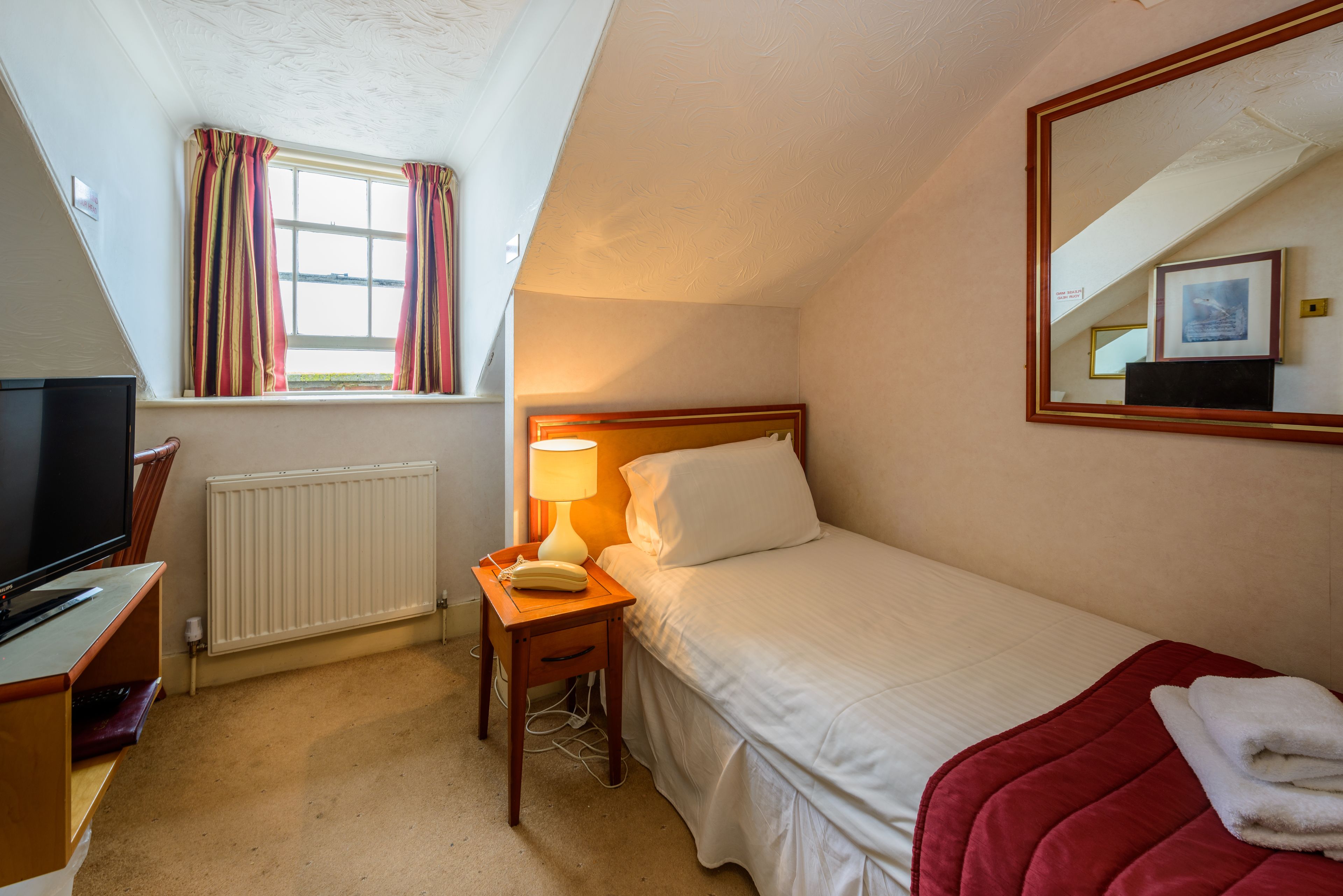 A hotel room with a bed, a bedside table with a lamp, a TV, and a window with curtains.