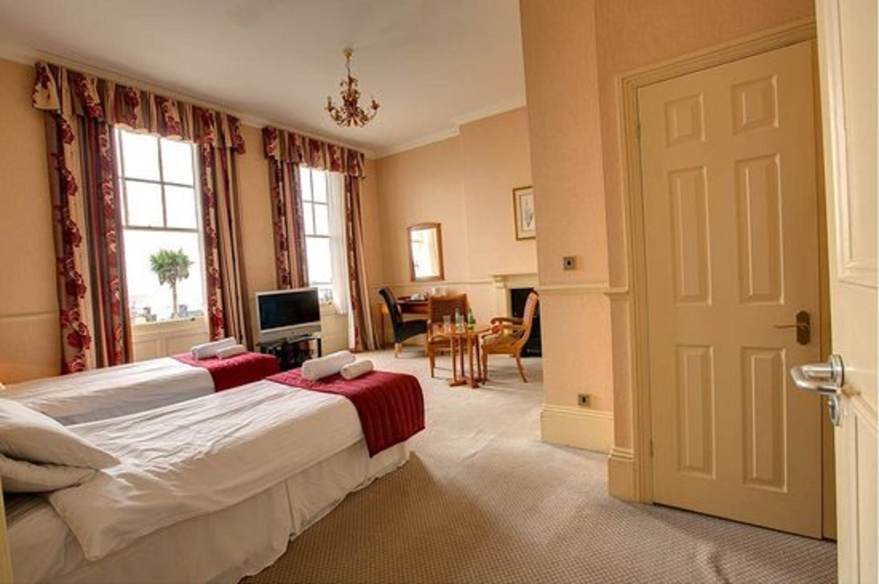A hotel room with two beds, a desk with a chair, a television, and a door.
