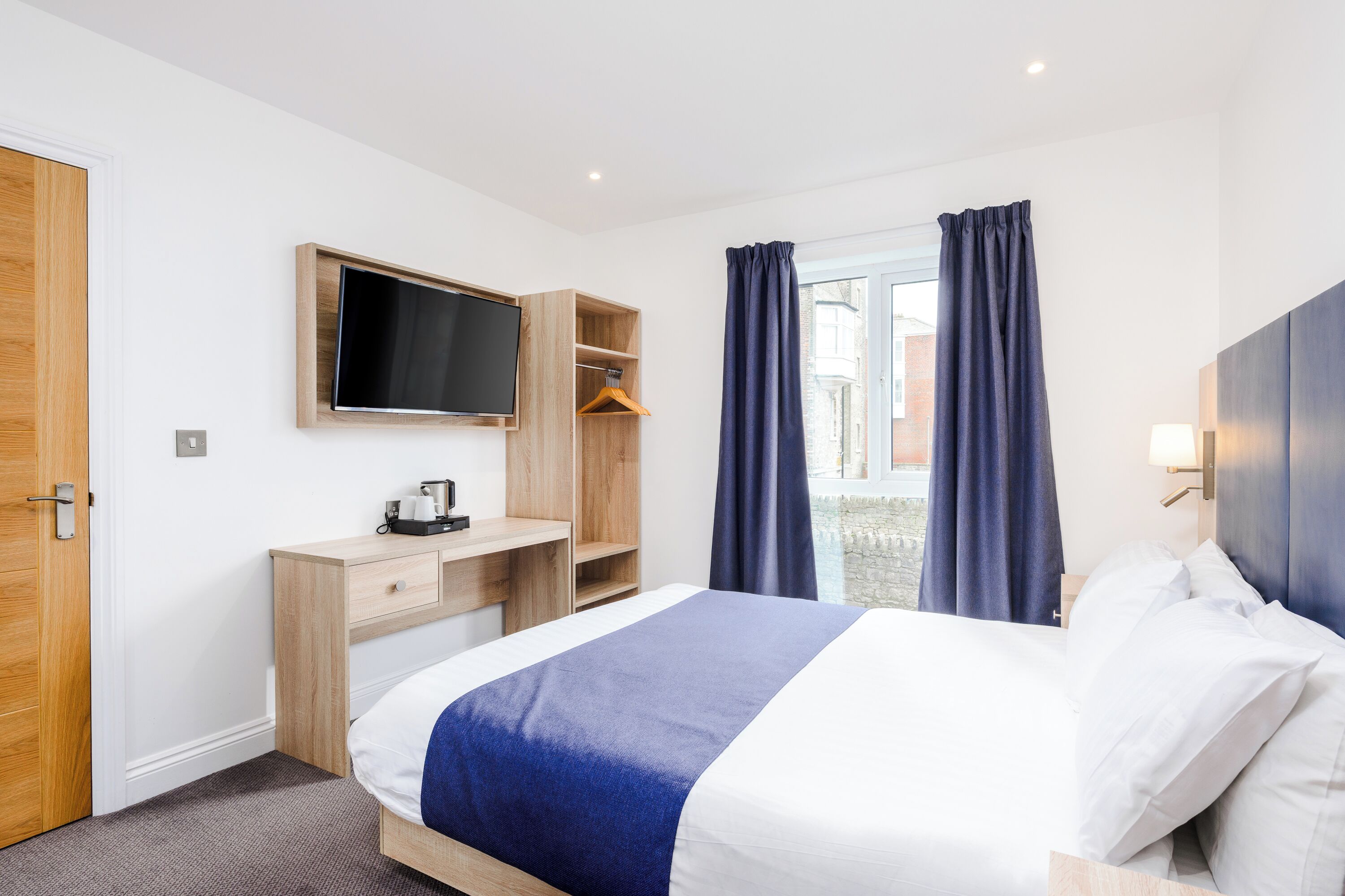 A hotel room with a bed, a desk, a TV, and a window with curtains.