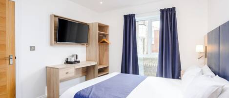 A hotel room with a bed, a desk, a TV, and a window with curtains.