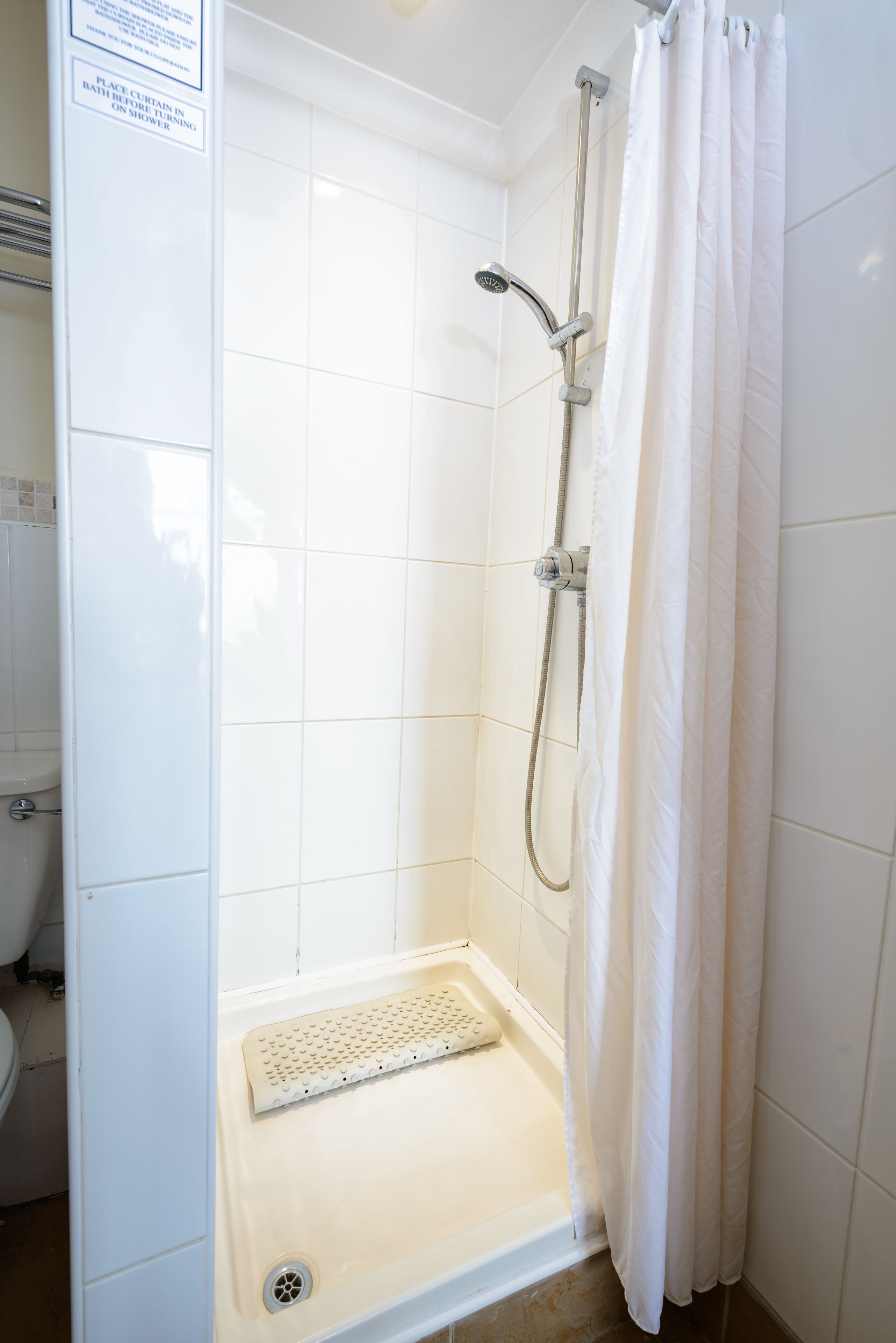 Ducha con cortina blanca, cabezal de ducha de mano y desagüe en el suelo.