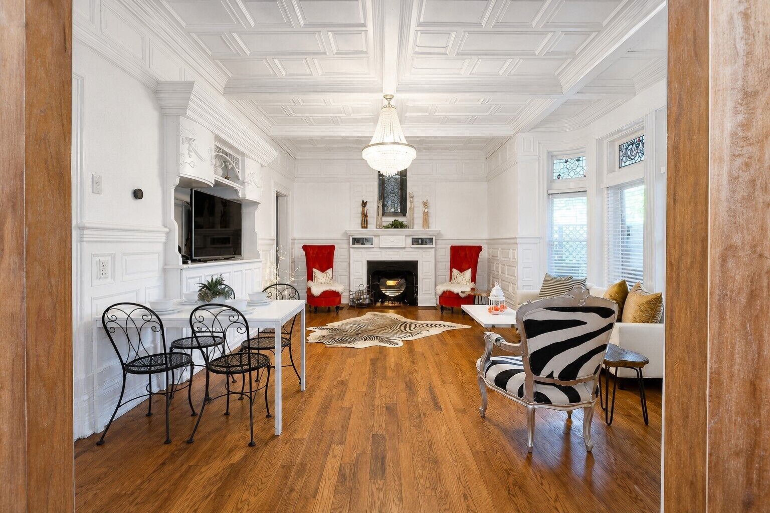 A spacious living room with a fireplace, a dining area with a white table and chairs, and a large chandelier.