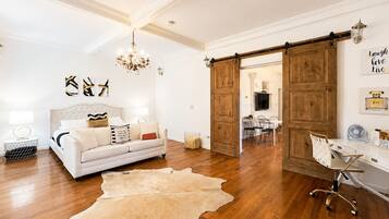 Um quarto com sofá branco, lustre, piso de madeira e porta corrediça rústica.