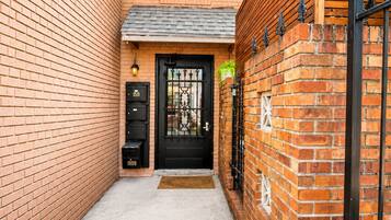 A narrow brick alleyway leading to a black metal gate with a door, flanked by brick walls and a small window above the door.