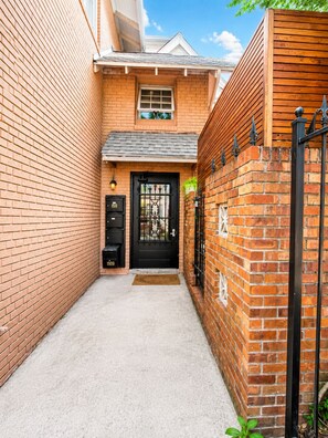 A narrow brick alleyway leading to a black metal gate with a door, flanked by brick walls and a small window above the door. - Unique , contemporary with HOT TUB!!! (Denver)