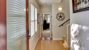 Un corridoio con pavimento in legno, una porta in vetro, un soffitto con faretti e un orologio a parete.