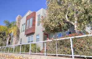 A modern two-story house with a stone chimney, a red door, and a white fence.