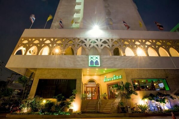 A building with a central entrance, multiple flags, and a well-lit facade.