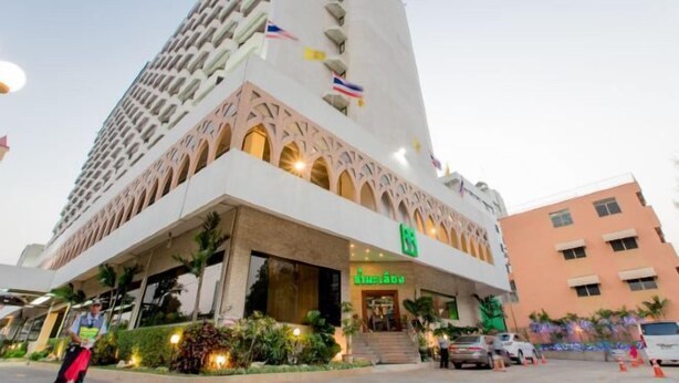 A hotel with a modern architectural design, featuring a prominent entrance with a green sign, and a large building in the background. - Mido Hotel (Bangkok)