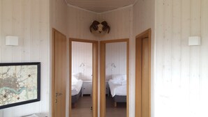 A corridor with wooden walls and doors leading to a room with two beds.