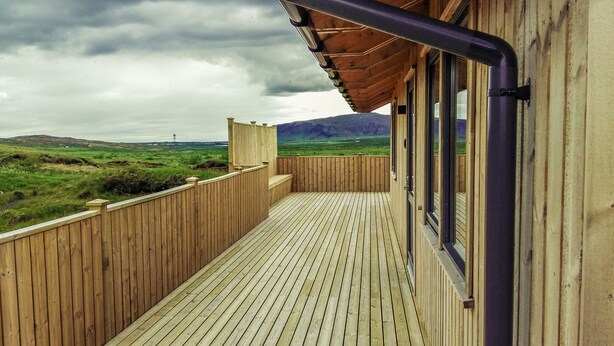 A wooden deck with a view of a green landscape and mountains.