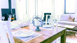 A dining area with a wooden table set for a meal, a white sofa, and large windows allowing natural light.
