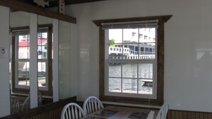 A dining area with a wooden table and white chairs, a window with a view of a waterfront and buildings, and a wooden ceiling with exposed beams. -  Houseboat in Boston Harbor Wifi A/C /Heat  Be rocked to sleep (boston)