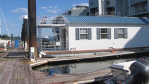 A docked boat with a white cabin and a blue roof, connected to a pier with a wooden deck. -  Houseboat in Boston Harbor Wifi A/C /Heat  Be rocked to sleep (boston)