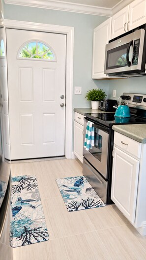 A kitchen with white cabinets, a microwave, a toaster, and a kettle. There are two wooden floors with patterned rugs. -  Beach time! Walk/Bike to Beach,Restaurants,Shops,fenced large backyard-sleeps 4 (Naples)