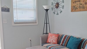 Una sala de estar con ventilador de techo, un sofá con cojines coloridos, una mesita auxiliar y una lámpara de pie.