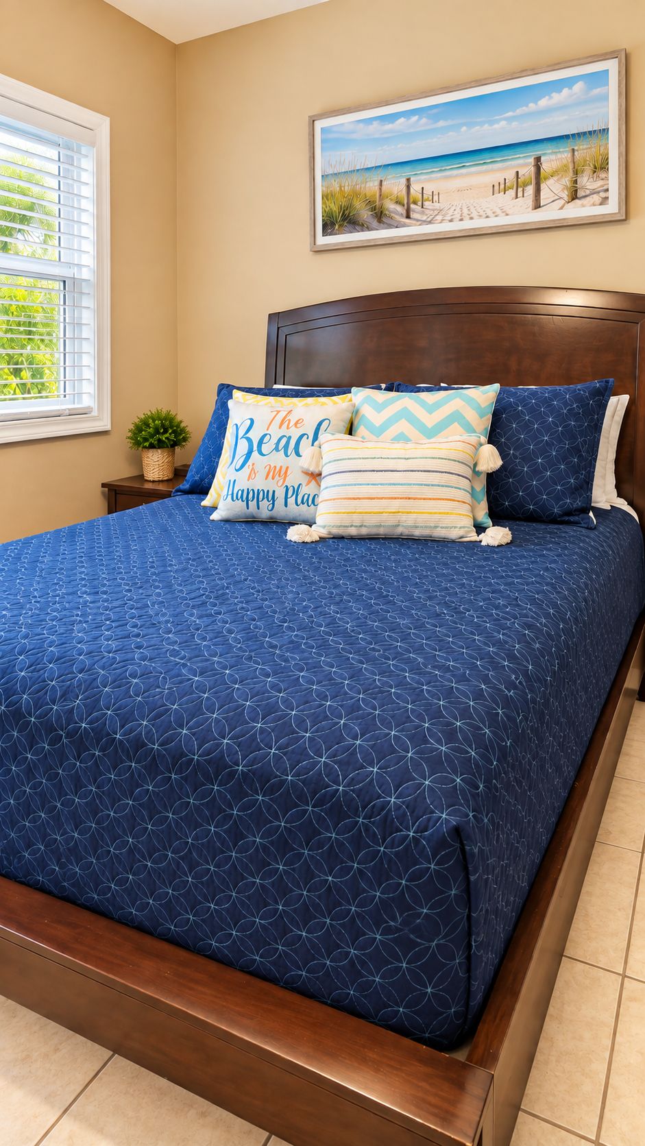 A bedroom with a bed, a headboard, a window, a wall-mounted painting, and a bedside table with a plant.